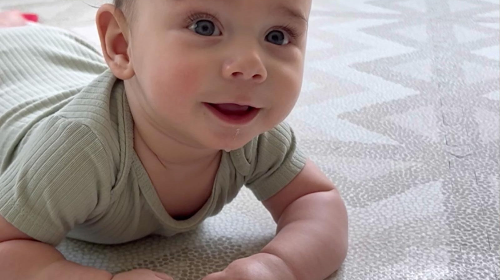 Baby lying on their belly on an Eeveve play mat during tummy time, lifting their head happily.