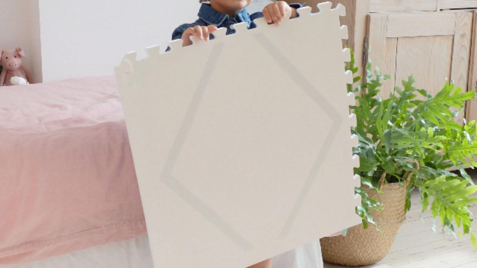 Child holding an Eeveve Beni Cashmere play mat tile, preparing to assemble the mat on the floor.
