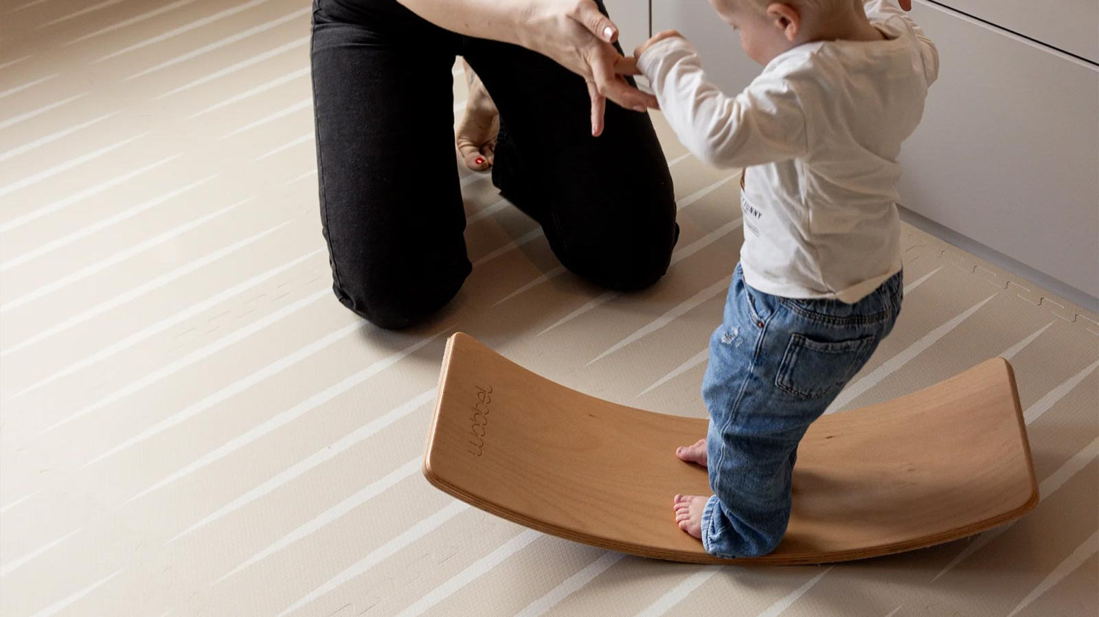 Mother playing with her toddler on an Eeveve play mat with a wooden wobble board.