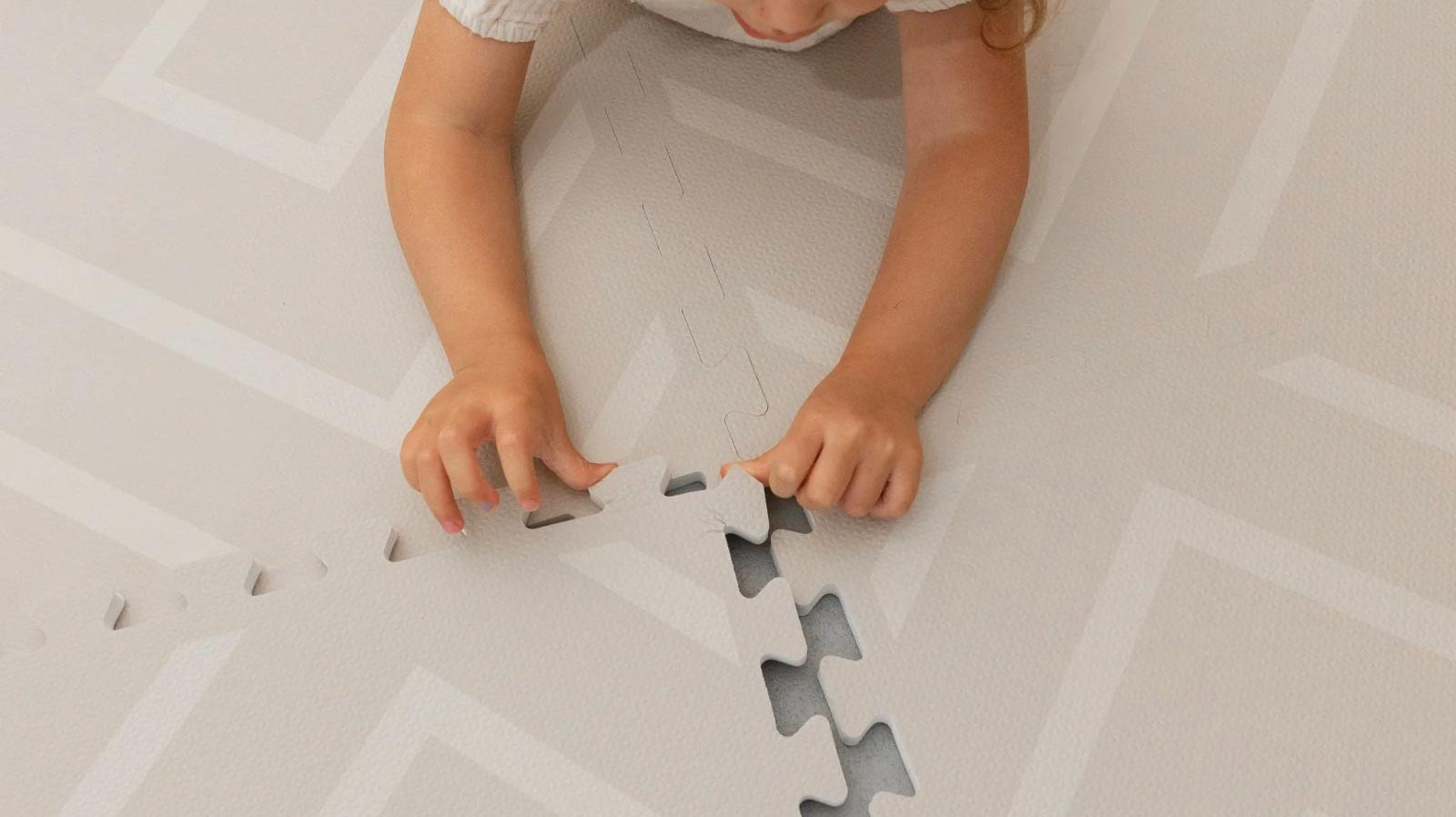 Toddler lying on their belly assembling the Eeveve Modern Blocks Dune play mat.