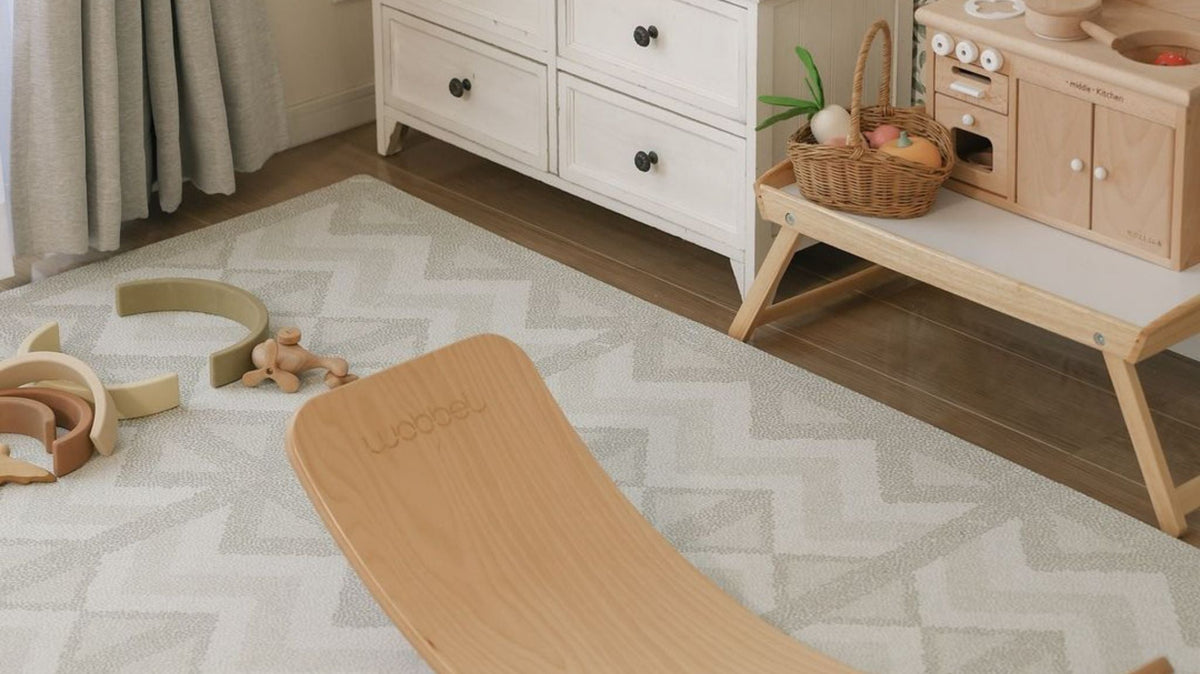 A patterned foam play mat laid across a living room floor in front of furniture, filling most of the open space