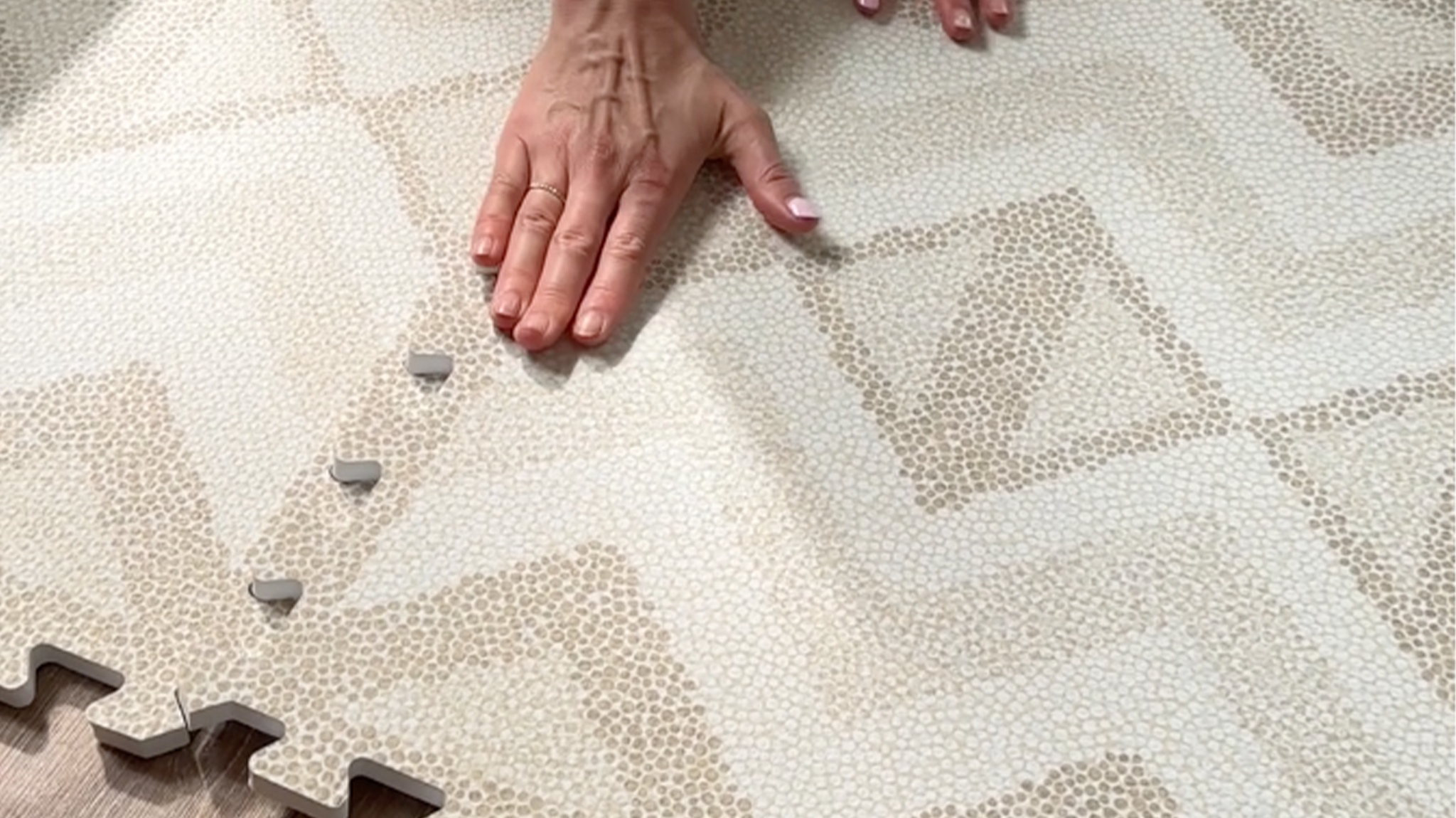 Close-up of hands connecting Eeveve Kilim Sand play mat tiles for a safe, stylish baby space.