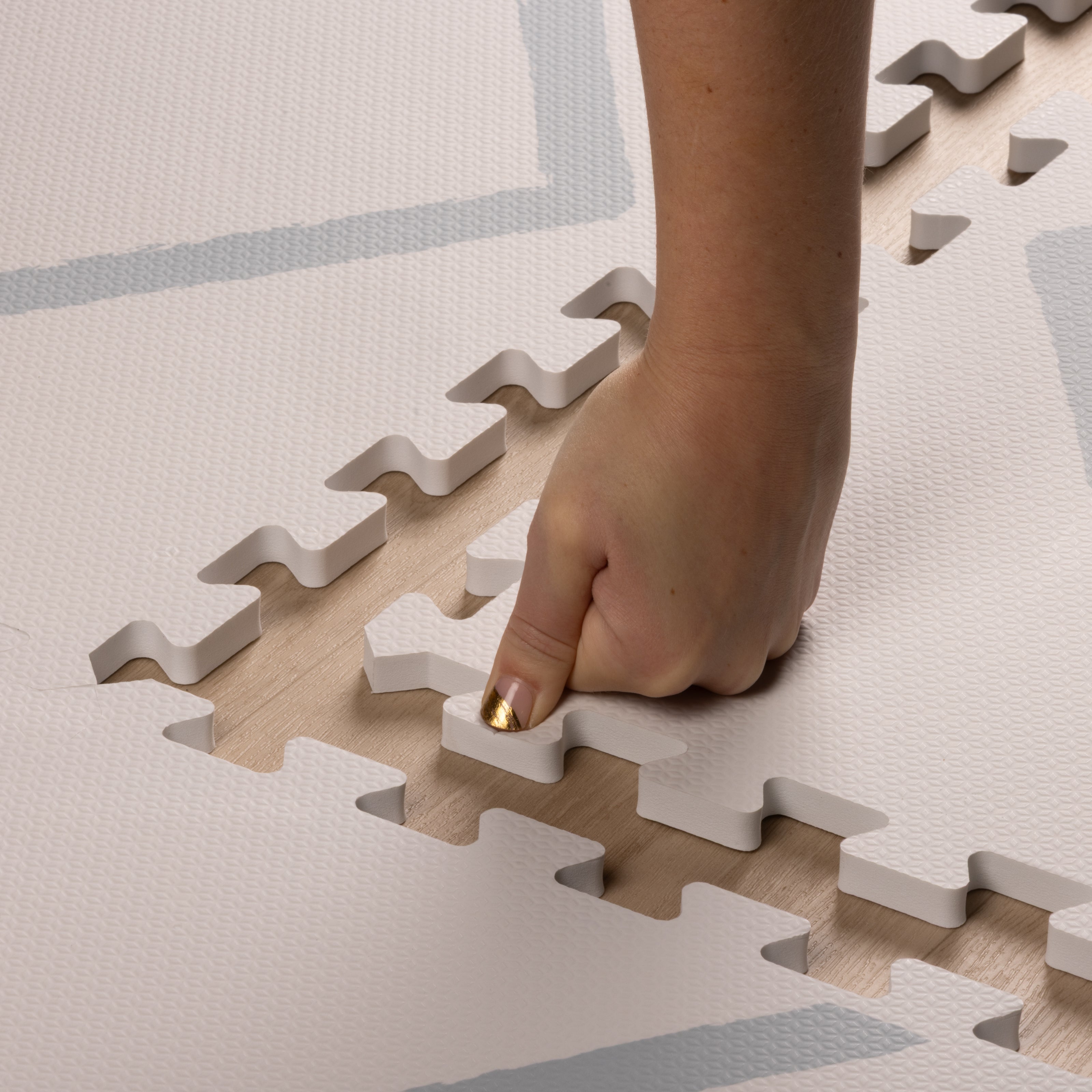 Hand pressing into the soft, non-toxic EVA foam of the Beni Powder Blue play mat, highlighting its safe and cushioned surface for babies.