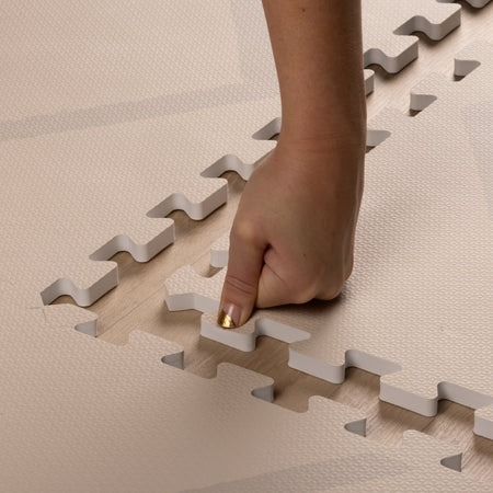 Hand pressing into the soft EVA foam of the Play Mat Beni Cashmere by Eeveve, showing its cushioned texture and easy assembly.