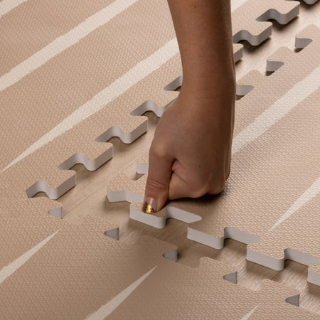 Close-up of hand assembling Lucio Desert Sand Play Mat, highlighting easy interlock and soft EVA foam texture.
