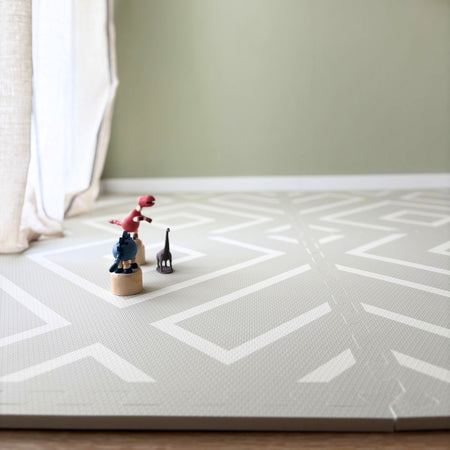 Low-angle view of the Play Mat Modern Blocks Soft Sage by Eeveve with toys on top, showcasing its safe, padded surface for crawling and playtime.