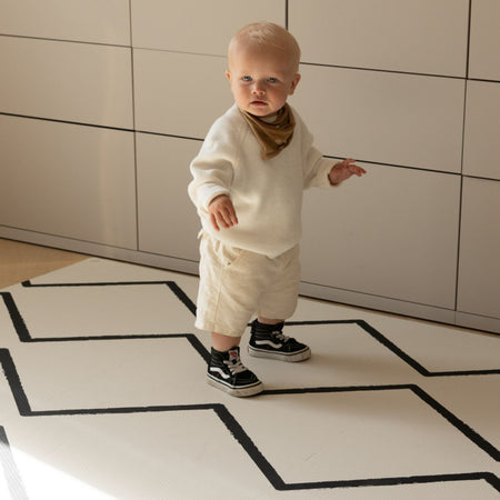 Toddler standing on Eeveve Beni - Ecru EVA foam play mat with black geometric pattern, ideal for safe indoor play and stylish nursery decor.