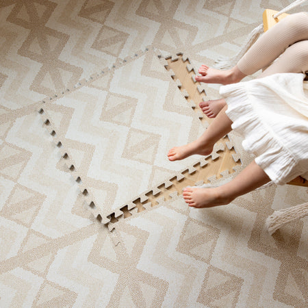 Child sitting on Kilim Sand Play Mat with one tile removed to show interlocking design. Soft, safe, and expandable EVA foam play mat.