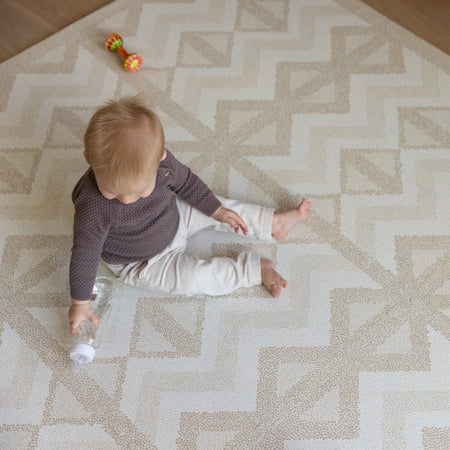 Baby sitting on Kilim Sand Play Mat holding a bottle. Soft EVA foam surface ideal for crawling, tummy time, and early play.