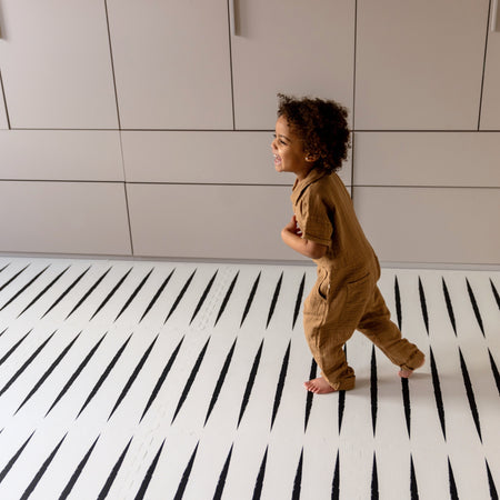 Toddler walking on Lucio Ecru EVA foam play mat with black stripes, providing a safe and cushioned surface for active play.