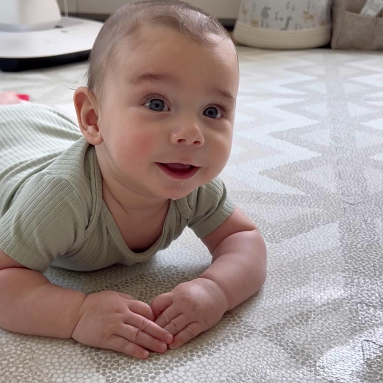Baby lying on their belly on an Eeveve play mat during tummy time, lifting their head happily.