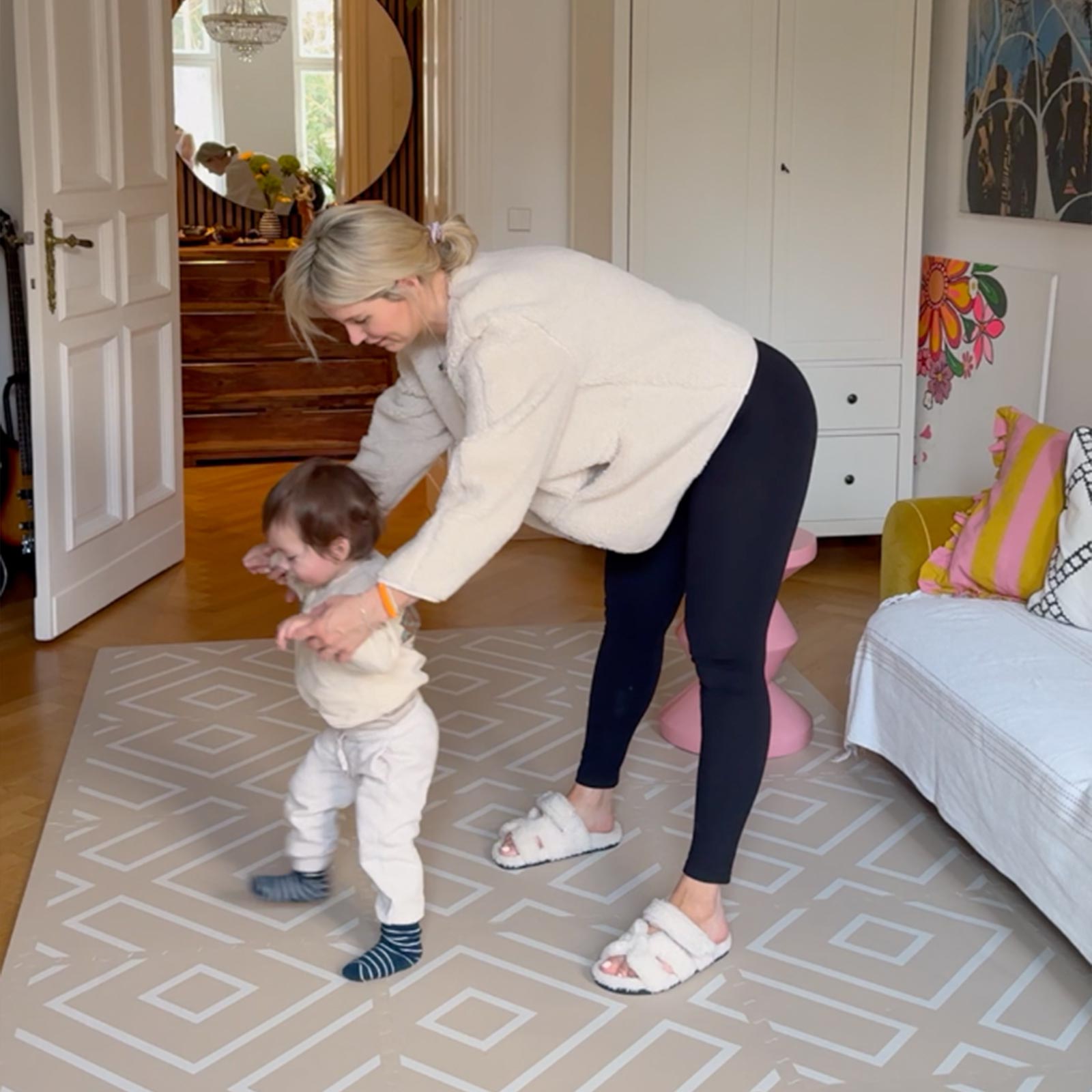 Mother guiding her toddler’s first steps on an Eeveve EVA foam play mat in a bright, modern living space.