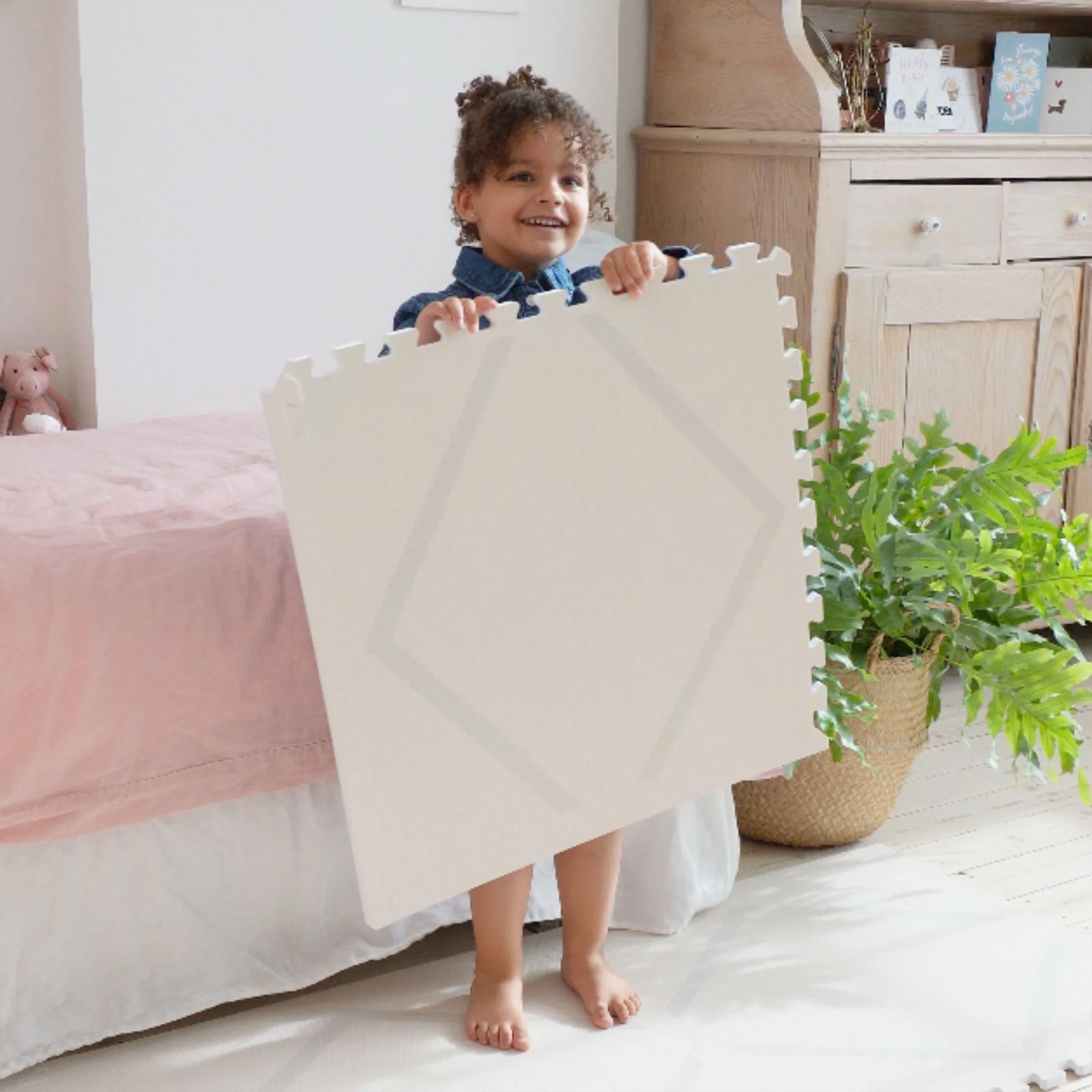 Child holding an Eeveve Beni Cashmere play mat tile, preparing to assemble the mat on the floor.