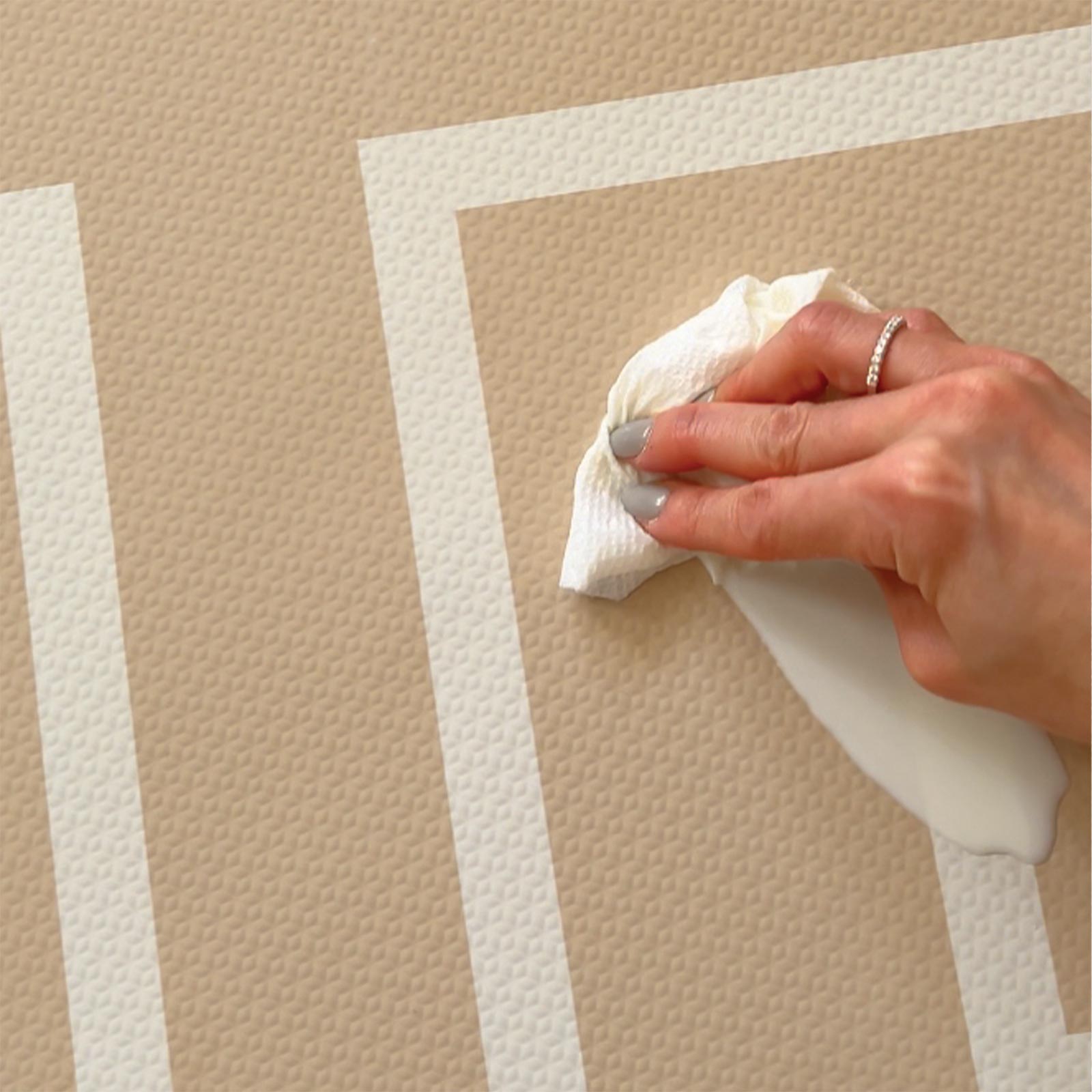 Eeveve Modern Blocks Desert Sand play mat being wiped clean after a small spill, showing its water-resistant surface.