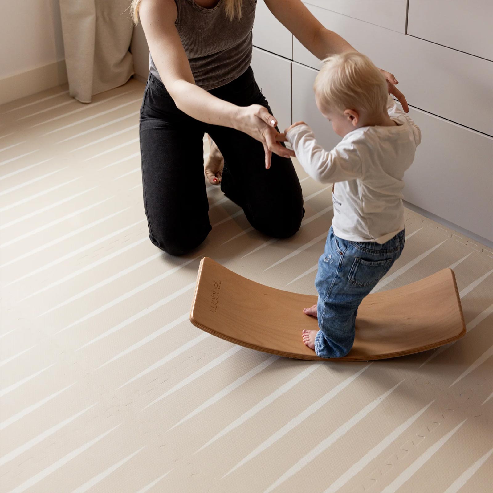 Mother playing with her toddler on an Eeveve play mat with a wooden wobble board.