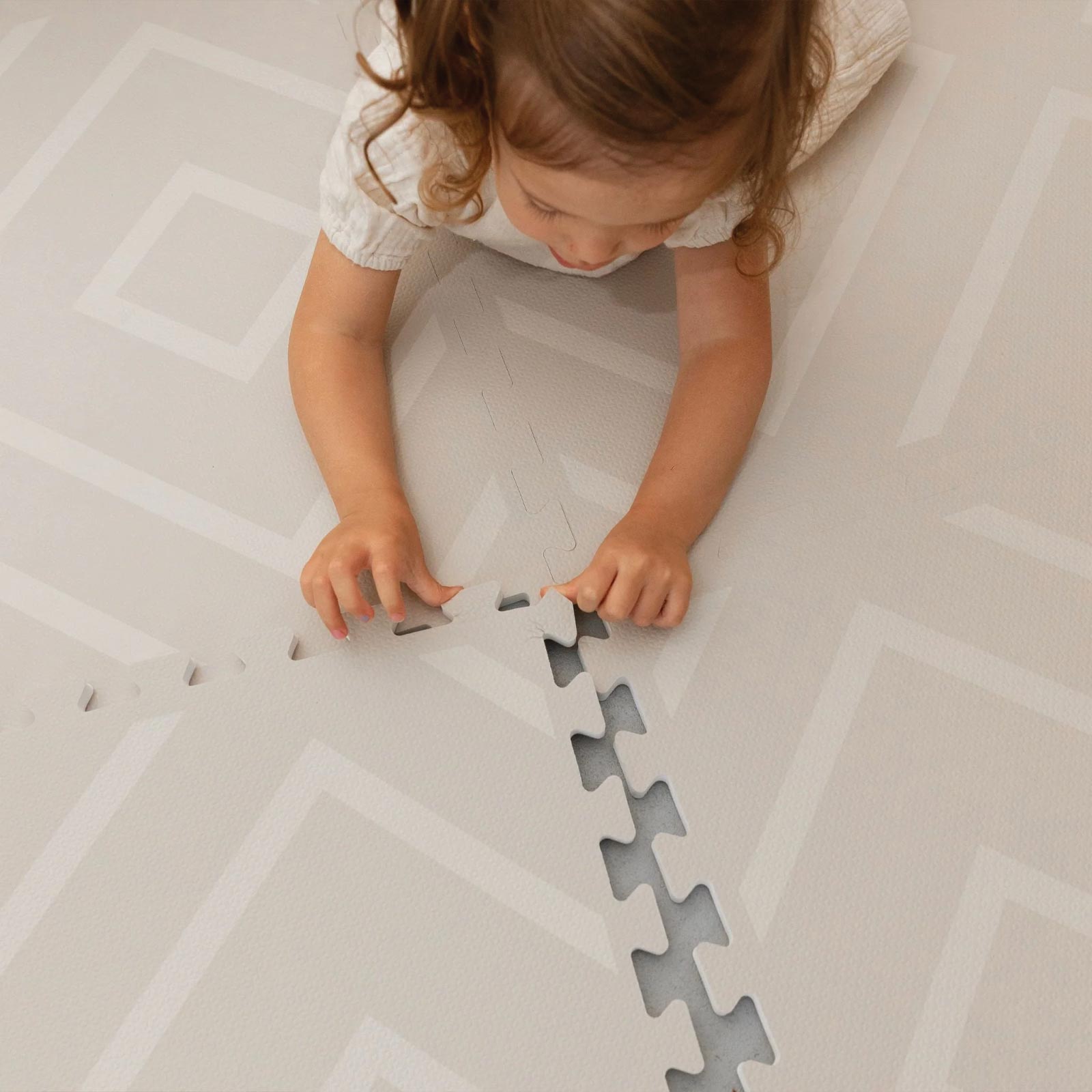Toddler lying on their belly assembling the Eeveve Modern Blocks Dune play mat.