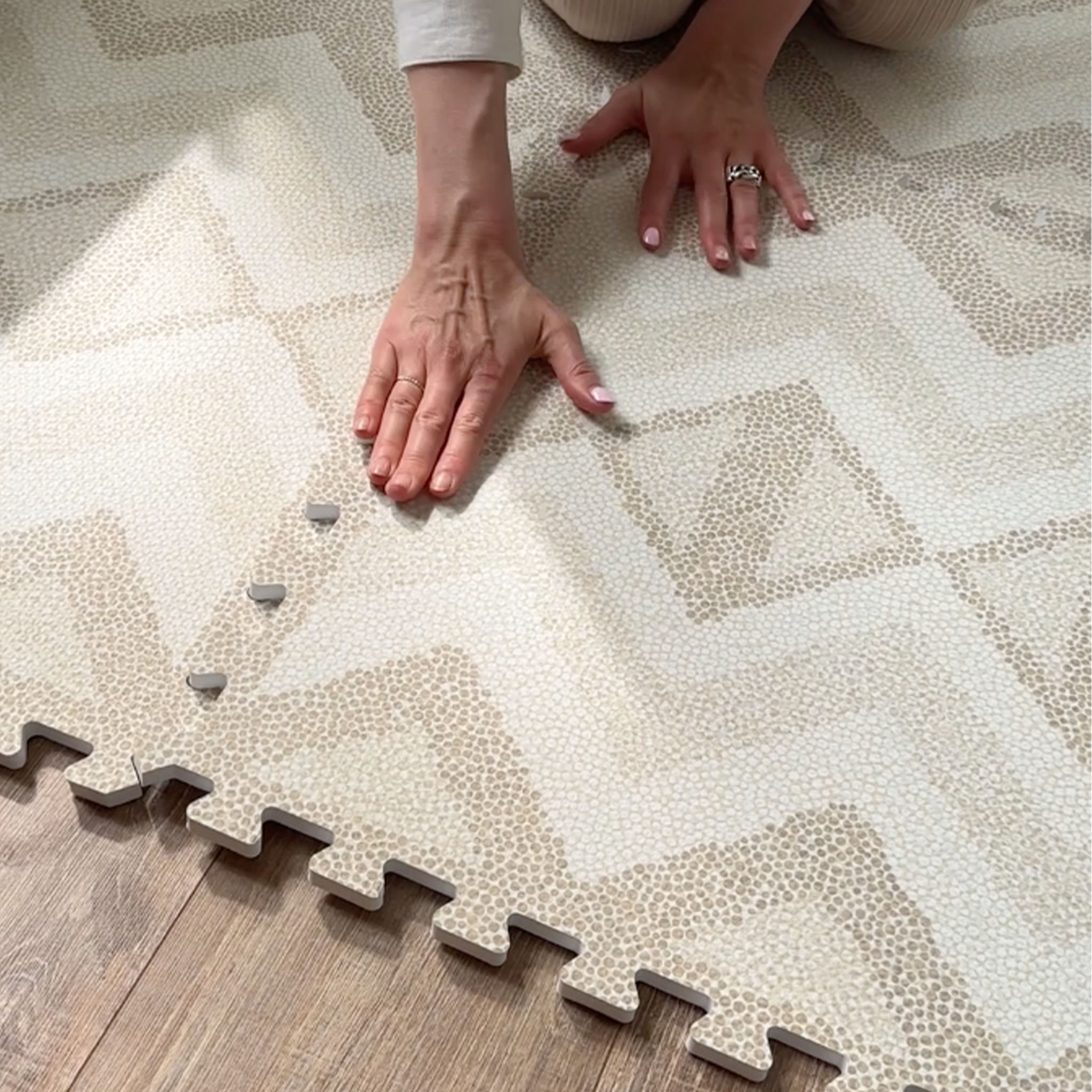 Close-up of hands connecting Eeveve Kilim Sand play mat tiles for a safe, stylish baby space.