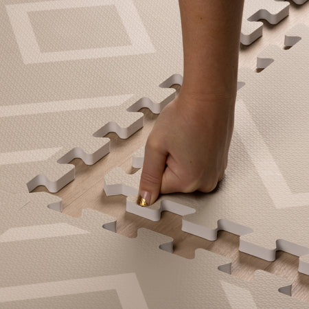 Hand pressing into the soft, cushioned surface of the Play Mat Modern Blocks Soft Sage, highlighting its EVA foam that meets US and EU toy safety standards and easy assembly.