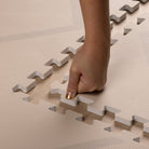 Hand pressing into the soft, non-toxic EVA foam of the Play Mat Beni Cashmere by Eeveve, showing its cushioned texture and easy assembly.