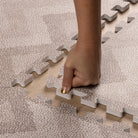 Close-up of hand assembling Eeveve Kilim Truffle play mat, highlighting soft EVA foam texture and secure interlocking design.