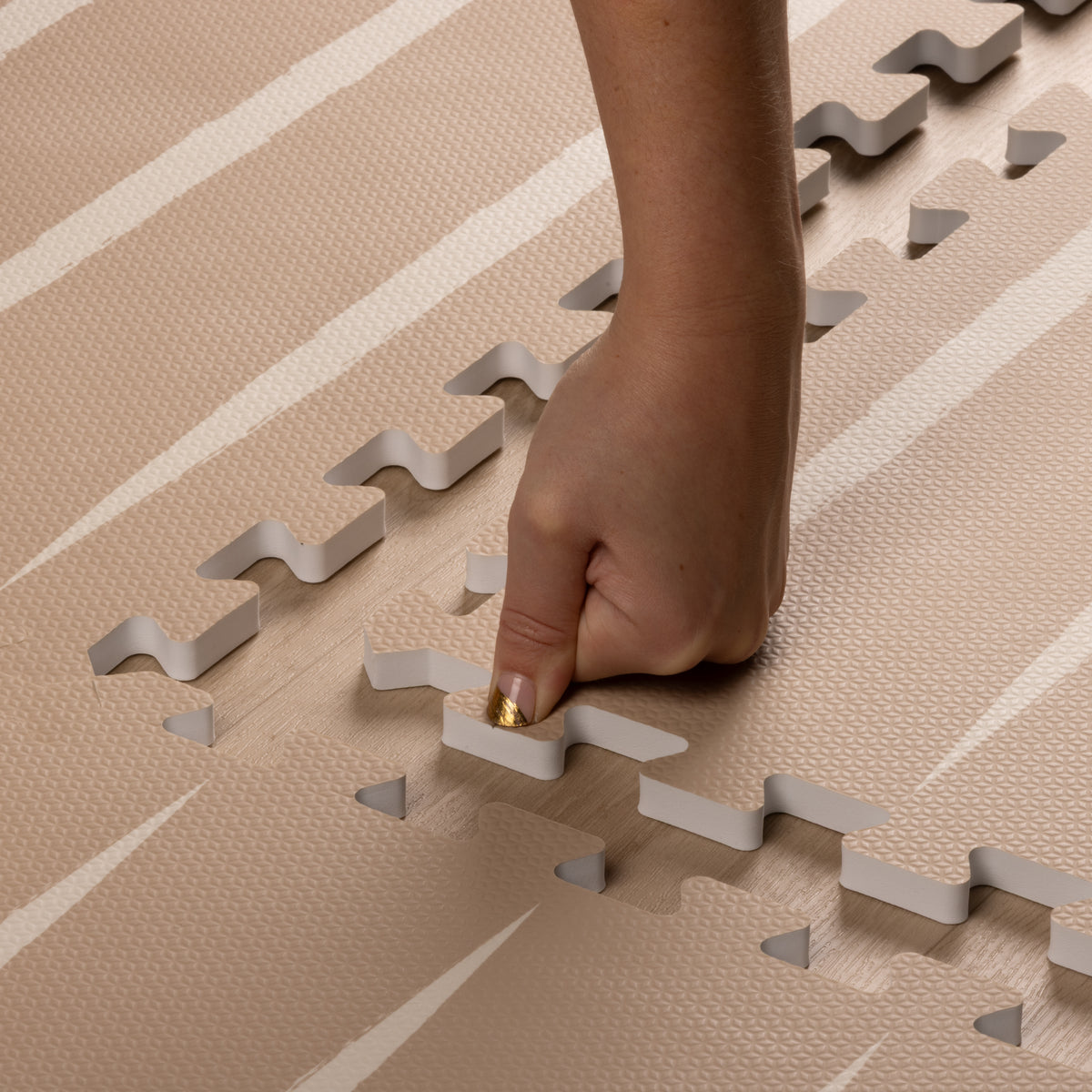 Close-up of hand assembling Lucio Desert Sand Play Mat, highlighting easy interlock and soft EVA foam texture.