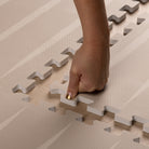 Close-up of hand assembling the Lucio play mat by Eeveve. Non-toxic EVA foam with secure interlocking design for easy setup.