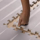 Close-up of hand assembling Lucio Nordic Mist play mat by Eeveve, highlighting soft, durable EVA foam and easy interlocking edges.