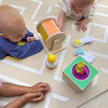 Two babies playing with toys on the Modern Blocks Play Mat. Cushioned surface supports safe crawling and sensory development.