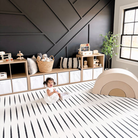 Lucio Ecru play mat by Eeveve in a modern nursery with a baby sitting on the EVA foam mat featuring black stripe design.