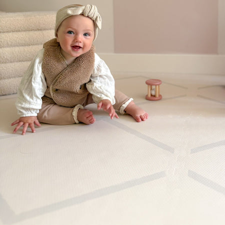 Smiling baby sitting on the Play Mat Beni Cashmere by Eeveve, designed for comfort and safety during tummy time and play.