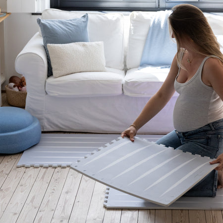Pregnant woman assembling Eeveve Lucio play mat in Nordic Mist, demonstrating easy setup of stylish, safe EVA foam tiles for baby spaces.