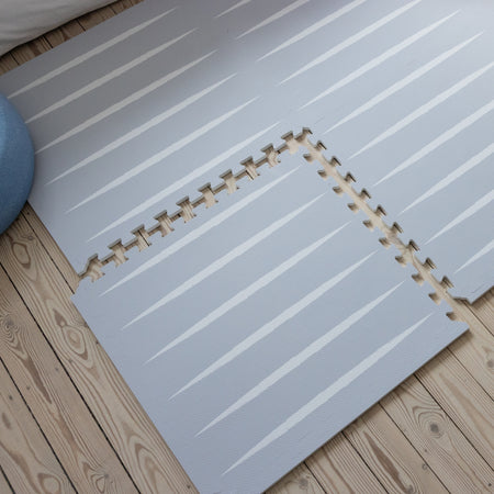 Partially assembled Lucio play mat in Nordic Mist on wooden floor, showing puzzle-like edges and modern striped design for baby-safe play.