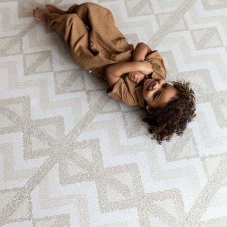 Toddler lying on Kilim Feather Gray Play Mat by Eeveve. Soft EVA foam mat with stylish pattern for safe and fun playtime.