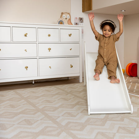Toddler sliding onto Kilim Sand Play Mat in a playroom. Safe, cushioned EVA foam mat with stylish geometric design.