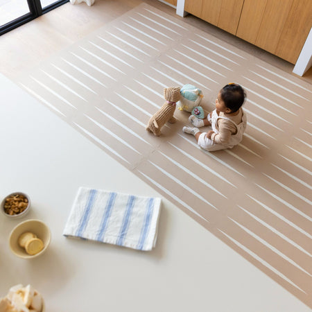 Lucio Desert Sand Play Mat by Eeveve with baby sitting and playing on EVA foam mat in modern living space.