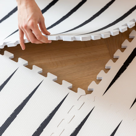 Hands assembling Lucio Ecru play mat tiles, demonstrating the easy interlock system for expanding play space in baby rooms.