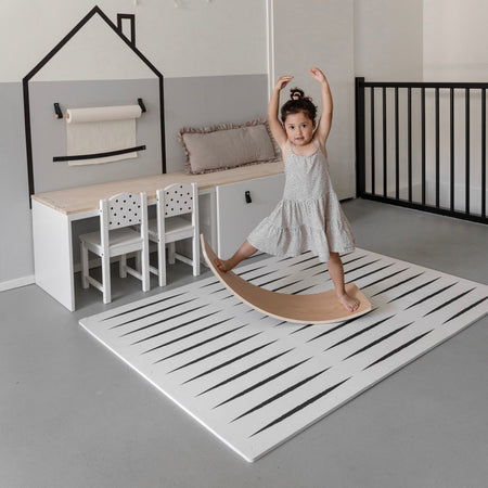 Child balancing on a wooden board atop the Lucio Ecru play mat, highlighting its thick, cushioned surface for toddler activities.